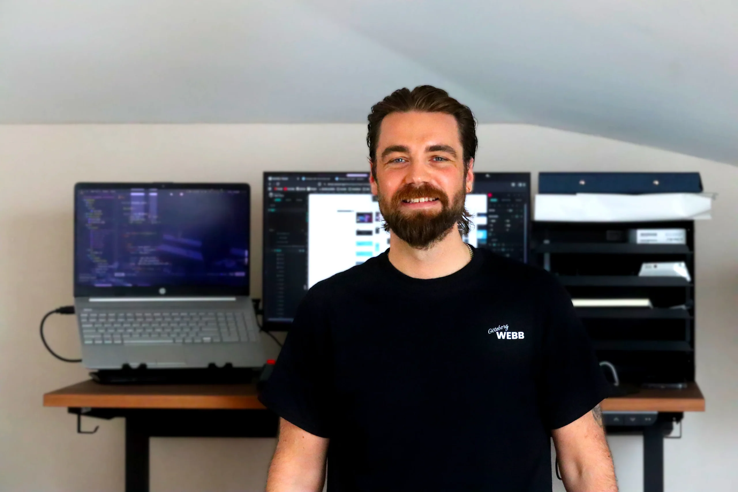 Leende man framför ett skrivbord med dataskärmar